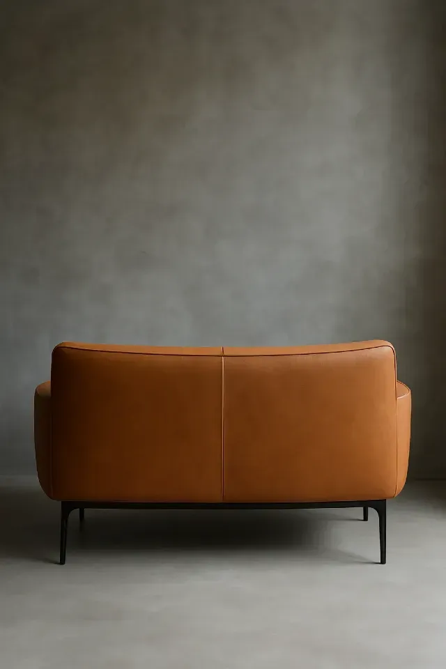 Canapé en cuir camel au design contemporain, dossier bas et lignes épurées, posé devant un mur en béton gris brut