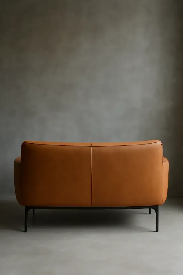 Canapé en cuir camel au design contemporain, dossier bas et lignes épurées, posé devant un mur en béton gris brut