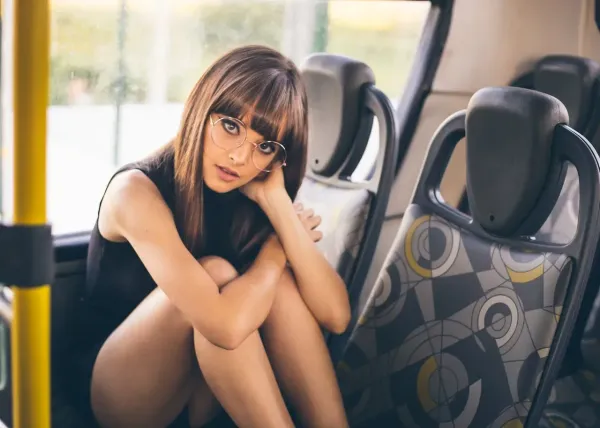 Jeune femme assise dans un bus, portant des lunettes rondes et une tenue noire, regard pensif